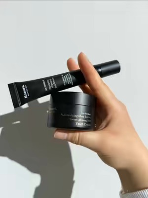 The image shows a close-up of a hand holding two skincare products, a tube and a jar, against a plain white background. It appears to be a UGC handheld product demo highlighting the items.