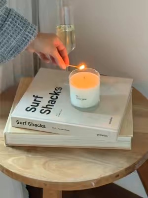 A hand lights a byrosiejane candle placed on top of two books, creating a cozy and inviting atmosphere.