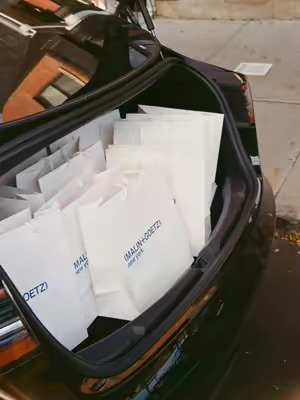 The image shows the trunk of a car filled with numerous shopping bags from Malin+Goetz. This suggests a large purchase or delivery, highlighting the brand's popularity and accessibility.